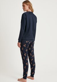 Marineblauwe katoenen longsleeve top gecombineerd met gestreepte pyjamabroek met herten en harten. Zachte textuur en geribde manchetten.