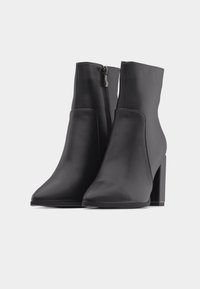 Μαύρα μποτάκια αστραγάλου με χοντρά τακούνια και πλαϊνά φερμουάρ, κατασκευασμένα από λεία δέρμα, τοποθετημένα δίπλα δίπλα σε απλό λευκό φόντο.