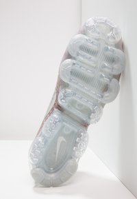 Zool van een Nike sportschoen met transparante, gesegmenteerde demping. Heeft een textuurpatroon en een lichte roze tint aan de zijkanten.