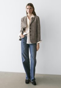 Brun hørblazer med hakskårne revers og sorte knapper, hvid skjorte med knapper, blå jeans med vide ben og sorte ankelstøvler.