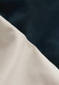 Két szövetmintázat találkozik egy szögben: az egyik sötét tengerészkék, a másik világos krém színű. Mindkettő sima, enyhén texturált felületű.