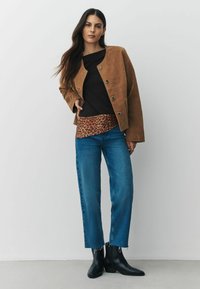 Barna velúr dzseki fémből készült gombokkal, fekete felső, leopárdmintás kiegészítő, kék egyenes szárú farmernadrág és fekete, hegyes orrú bokacsizma.