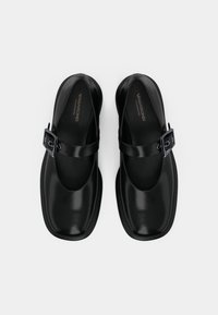 Black leather Mary Jane shoes with a squared toe, wide strap, and rectangular buckle accent. Smooth texture and minimalistic design.