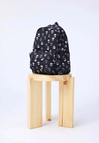 Zaino nero con un motivo ripetuto di facce aliene in bianco e grigio. Il bag ha una tasca frontale e una maniglia superiore.
