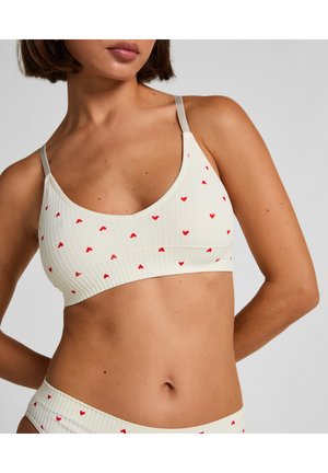 Licht crèmekleurige bralette met kleine rode hartjes, geribbelde textuur en dunne, verstelbare bandjes. Gecombineerd met bijpassend broekje.