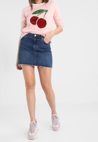 Rosa långärmad skjorta med pälsglittert körsbärsdesign, matchad med en blå denim minikjol med fransar och ljusrosa sneakers.