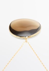 Pendente dorato con una pietra ovale a sfumatura marrone, caratterizzata da una superficie liscia e una catena per il pendente. Design semplice con accenti minimali.