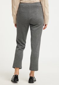 Grijze, gestructureerde broeken met een subtiel ruitpatroon, strakkend op de taille, taps toelopende pijpen en een cropped lengte. Draagt zwarte schoenen.