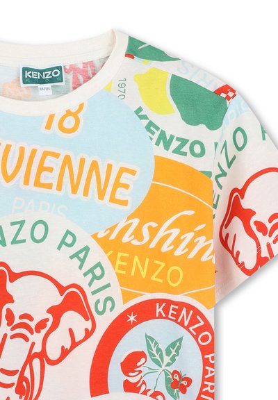T-shirt en coton blanc avec des imprimés graphiques colorés, incluant un éléphant et des homards, ainsi que divers motifs de texte en orange, vert et bleu.
