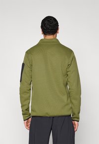 Πράσινο ελαφρώς υφασμένο τζάκετ fleece με γιακά, μαύρη λεπτομέρεια στο αριστερό μανίκι και ίσιο τελείωμα. Διαθέτει άνετη εφαρμογή.