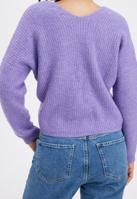 Fioletowy sweter z dzianiny o fakturowanej strukturze, z dekoltem w serek i długimi rękawami, w połączeniu z jasnoniebieskimi, wysokim stanem jeansami z klasycznymi kieszeniami.