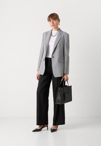 Šedý elegantní blejzr, bílý top, černé široké kalhoty a černá strukturovaná kabelka. Špičaté černé lodičky, vrstvený stříbrný náhrdelník.