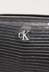 Black crocodile-patterned leather bag with silver metal hardware and a prominent "CK" logo. Features a top zipper closure.