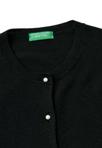 Černý pletený kardigan s kulatým výstřihem, dvěma bílými knoflíkovými uzávěry a štítkem s nápisem "UNITED COLORS OF BENETTON."