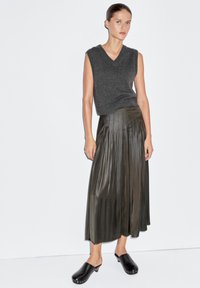 Top senza maniche grigio in maglia abbinato a una gonna plissettata verde oliva, caratterizzata da un design fluente. Il look è completato da zoccoli neri con dettagli argentati.