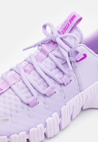 Světle fialová běžecká bota Nike Free s texturovanou podešví, síťovaným svrchním materiálem, smyčkovými tkaničkami uvázanými do mašle a s označeným poutkem na jazyku.
