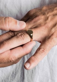 Gouden ring met een druppelontwerp, gepolijste oppervlakte, gedragen op een hand. Huidtextuur en subtiele details van de vingers zijn zichtbaar. Witte achtergrond.