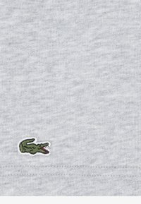 Gråt bomuldsstof med en lille grøn broderet krokodillelogo nær kanten, med en subtil tekstur og en glat finish.