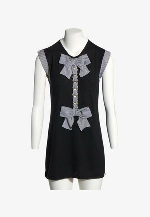 Robe noire sans manches avec des nœuds en tissu rayé et un volant froncé devant, présentée sur un mannequin blanc avec un fond uni.