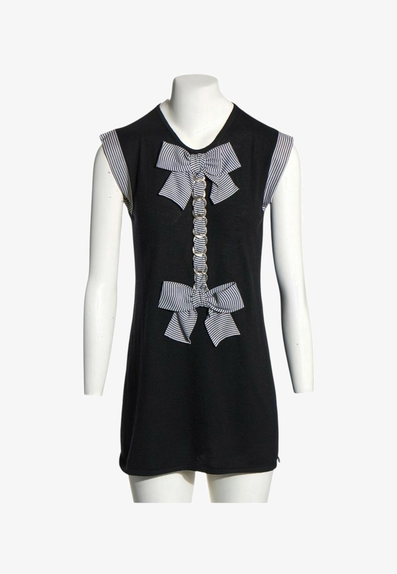 Robe noire sans manches avec des nœuds en tissu rayé et un volant froncé devant, présentée sur un mannequin blanc avec un fond uni.