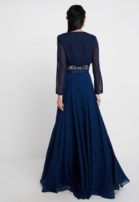 Abito lungo blu navy con maniche lunghe trasparenti, un corpetto aderente decorato con pizzo floreale e una gonna fluente.