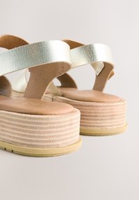 Platformsandaler med metalliske sølvremme, en struktureret beige fodbænk og en stribet lysebrun platformsål. Skridsikker gummiydersål.