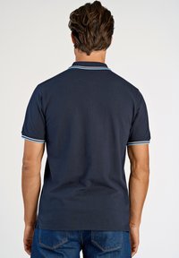 Mörkblå pikétröja med kort ärm, med en kontrasterande ljusblå krage. Tillverkad av bomullsblandning, med en mjuk textur och avslappnad passform.