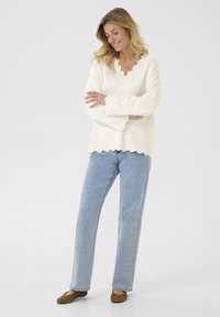 Crème kleurige trui met een gekartelde halslijn en manchetten, gecombineerd met lichtblauwe straight-leg jeans en bruine flats. Eenvoudig, casual ontwerp.