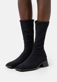 Svarta ankelboots i stretchmaterial med spetsig tå och blockklack. Har en samlad textur längs skaftet för extra detalj.