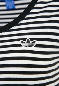 Camiseta de algodón a rayas blancas y negras con cuello redondo y un logotipo bordado en el centro. Textura suave y patrón uniforme.