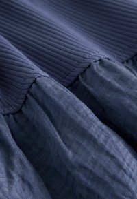 Gros plan sur un tissu bleu foncé avec une texture en maille côtelée en haut et un matériau froncé semblable au lin en bas formant une couture.