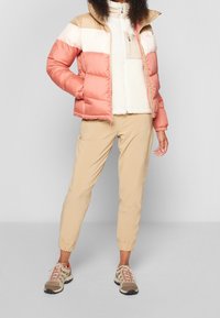 Kurtka pikowana w paski koralowe, kremowe i beżowe; wysoki kołnierz; wnętrze z polaru. W połączeniu z beżowymi zwężanymi spodniami i brązowymi trampkami.