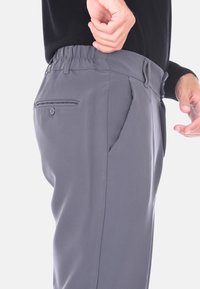 Uomo che aggiusta la vita di pantaloni grigi con tasca posteriore con bottone e tasca laterale, indossando un top nero.