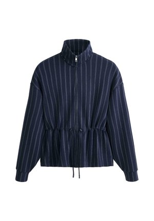 Temno modra jakna na zadrgo z belimi navpičnimi črtami, visokim ovratnikom, dolgimi rokavi in nastavljivim pasom z vrvico.