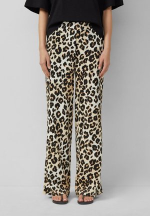 Szerokie spodnie z nadrukiem w cętki lamparta noszone z czarnym topem i czarnymi sandałami, stojąca na jednolitym jasnoszarym tle.