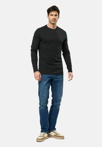 Chemise noire à manches longues avec un col rond, assortie à un jean en denim bleu. Les chaussures sont beige et blanches avec un design sportif.