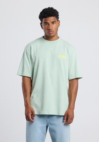 Mint green cotton t-shirt with short sleeves. Features yellow "NYC" lettering on the chest, relaxed fit, and a smooth texture.