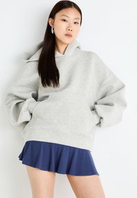 Grey oversized hoodie made from soft fabric, featuring a spacious front pocket and drawstring hood, paired with a navy ruffled skirt.