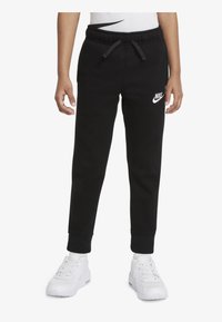 Pantalones de chándal negros con cintura elástica, cordón y puños, con un logo blanco de Nike en la pierna izquierda. Combinados con zapatillas blancas.