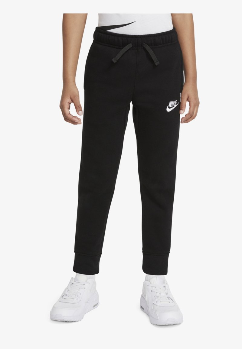 Pantalones de chándal negros con cintura elástica, cordón y puños, con un logo blanco de Nike en la pierna izquierda. Combinados con zapatillas blancas.