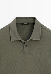 Olijfgroene polo shirt gemaakt van zachte katoen, met een kraag, twee knopen en een subtiele ribbelstructuur.