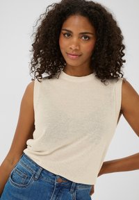 Haut en tricot sans manches beige avec un col rond, présentant une texture douce et une coupe ample, associé à un jean en denim bleu.