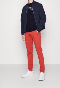 Chaqueta bomber de la marina sobre un sudadera negra con gráfico blanco, combinada con pantalones ajustados rojos y zapatillas blancas.