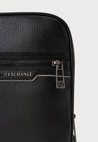Zwarte textuur vegan leren tas met een ritssluiting. Kenmerkt een zilveren logo-detail en contrasterende witte stiksels langs de rits.