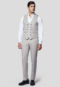 Jasnoszary, trzyczęściowy garnitur z kamizelką i dopasowanymi spodniami, z pięcioma guzikami i subtelną fakturą, zestawiony z białą koszulą i czarnymi butami.
