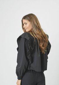Blusa nera con maniche a ruffle, design cropped e polsini elasticizzati. Tessuto liscio su uno sfondo neutro.
