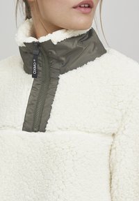 Witte fleece pullover jas met olijfgroene nylon accenten, hoge kraag en ritssluiting. Gelaagd, zacht materiaal en contrasterend kleurblokontwerp.
