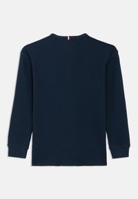 Camisa de manga larga azul marino con un patrón texturizado tipo waffle, escote redondo y puños acanalados. Presenta un pequeño detalle rojo en la parte trasera.