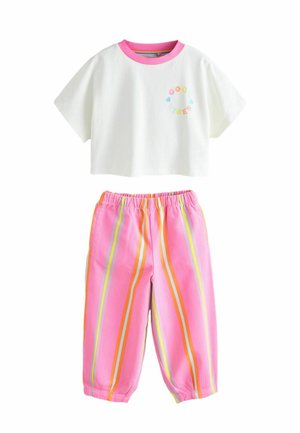 T-shirt blanc court avec col rose et texte "Good Vibes" ; pantalon rose ample avec rayures verticales orange et jaunes et taille élastique.