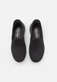Black mesh slip-on shoes with a smooth rubber sole, featuring elastic side panels and "SKECHERS slip-ins" branding on the insole.